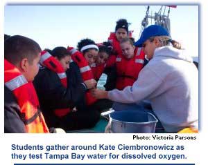 Students gather around Kate Ciembronowicz as they test Tampa Bay water for dissolved oxygen